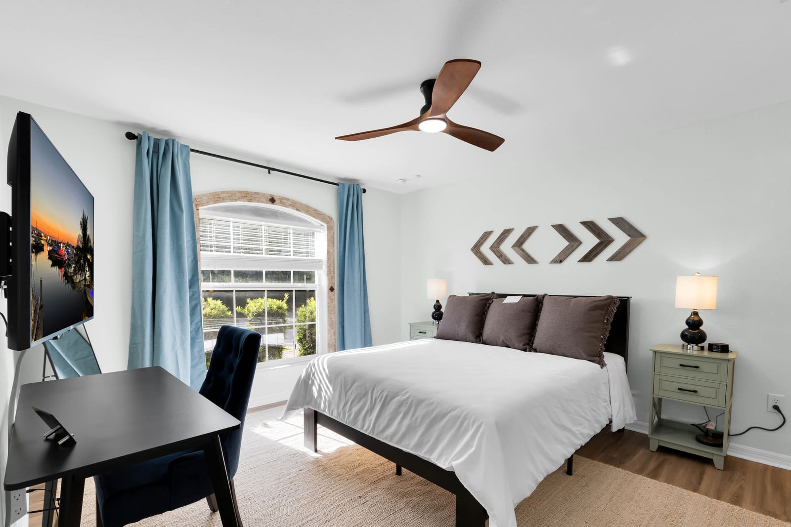 Bedroom with queen bed, blue curtains, desk, and TV
